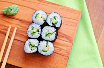 Vegetarian sushi roll with chopsticks on wooden cutting board.