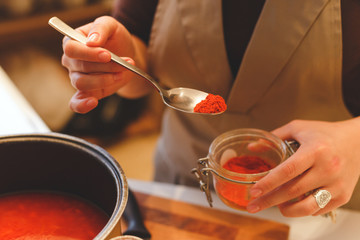 Spoon with spices in the hands of a girl cooking tomato soup close up.
