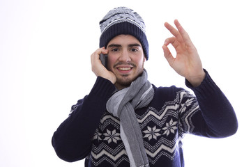 Young man with sweater and scarf talking on the mobile phone making the ok sign