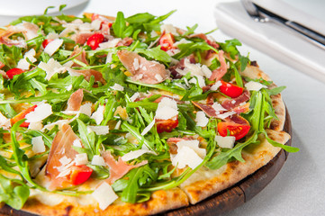 Selective focus Close up Delicious Pizza with hamon and cherry tomato slices, parmezan cheese and arugula on the wooden board on the served restaurant table
