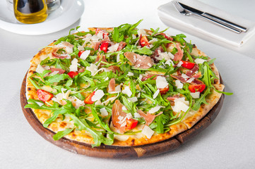 Selective focus Close up Delicious Pizza with hamon and cherry tomato slices, parmezan cheese and arugula on the wooden board on the served restaurant table