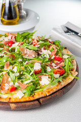 Selective focus Close up Delicious Pizza with hamon and cherry tomato slices, parmezan cheese and arugula on the wooden board on the served restaurant table. Top view