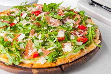 Selective focus Close up Delicious Pizza with hamon and cherry tomato slices, parmezan cheese and arugula on the wooden board on the served restaurant table