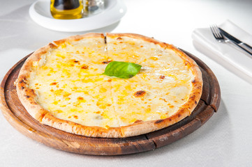 Four cheese pizza quattro fromaggi with basil leaf on a rustic wooden board on the served restaurant table