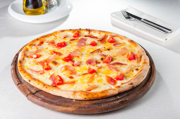 Selective focus hot meat Pizza with hamon, cheese and cherry tomatos on the wooden board on the served restaurant table
