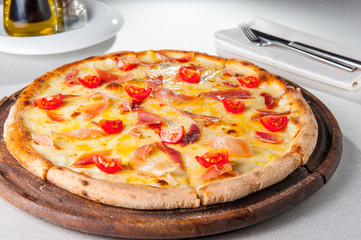 Selective focus hot meat Pizza with hamon, cheese and cherry tomatos on the wooden board on the served restaurant table