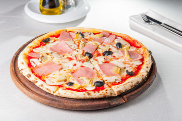 Selective focus Close up Delicious Meat Pizza with bacon, chicken fillet, sliced mushrooms and olives on the wooden board on the served restaurant table