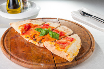 Close up Traditional Italian closed pizza Calzone on the wooden board on the served restaurant table. Selective focus.