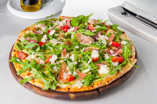 Selective focus Close up Delicious Pizza with hamon and cherry tomato slices, parmezan cheese and arugula on the wooden board on the served restaurant table