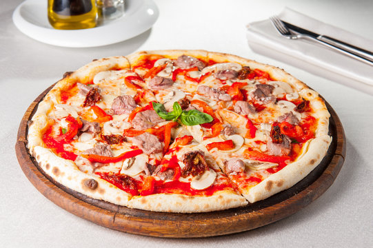 Tasty, flavorful Pizza with veal and mushrooms on the wooden board on the served restaurant table
