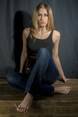 Fototapeta na wymiar Beautiful long-haired young blonde woman in a black tank top and jeans sitting on a chair 