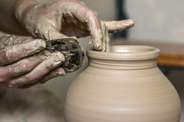 Fototapeta na wymiar Making Crock crude wet close-up. Man hands and tool making clay jug macro. The sculptor in the workshop makes a jug out of clay closeup. Vase of white clay crude wet closeup,