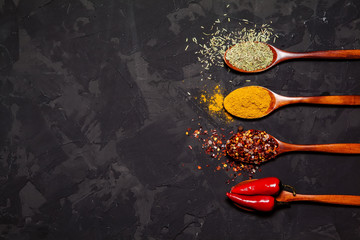 Colorful spices in spoons on dark black background, Top view. Food and cuisine ingredients.