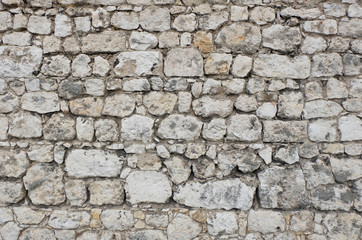 Antique stone wall of an ancient fortress / castle, mainly white and light colored stone blocks of varying sizes and shapes, creating an individual pattern / texture.