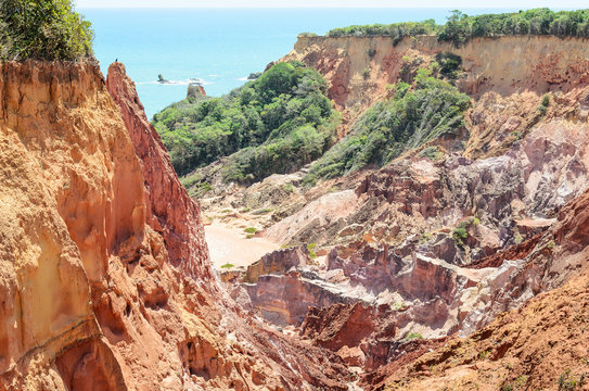 Canyon of cliffs with many stones sedimented by time, rocks with red and yellow colors and the sea in the background. Cliffs of Coqueirinho beach, PB - Brazil.
