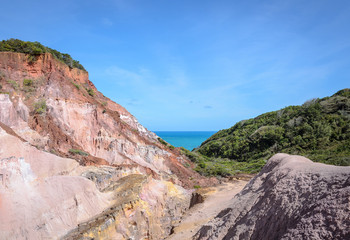 Canyon of cliffs with many stones sedimented by time, rocks with red and yellow colors and the sea in the background. Cliffs of Coqueirinho beach, PB - Brazil.