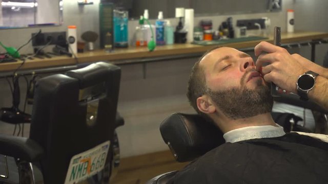 Barberman shaving beard of man