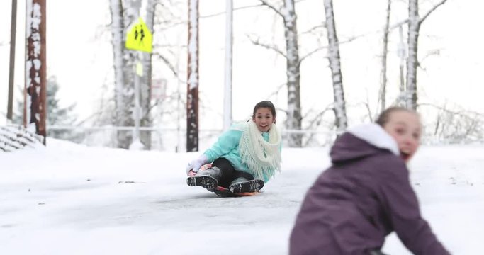 Two girls riding down an icy hill on snow sleds