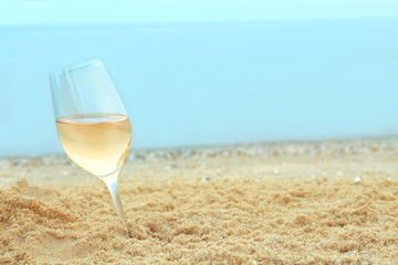 Glass of wine on sand on sea background