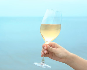Female hand holding glass of wine on sea background