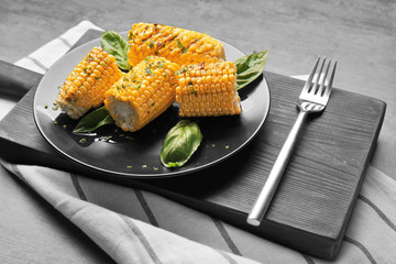Kitchen board with plate full of cut tasty grilled corncobs on wooden table