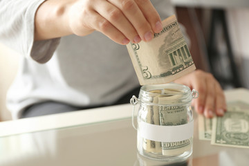 Female hand putting money into glass jar closeup