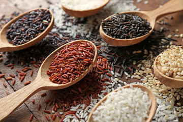 Different types of rice in spoons on wooden table closeup