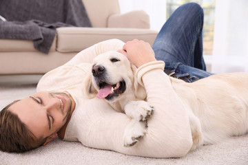 Obraz premium Handsome man with dog lying on carpet at modern room interior