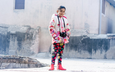 Portrait of Cute Indian Girl with camera wearing Jacket against old grungy wall outdoor