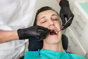 Dentist examines  tooth  with mouth mirror. Male patient's  at the  chair open-mouthed and close up. Oral hygiene
