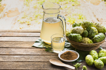 Noni fruit and noni juice with noni powder and wooden spoon on wooden table.Fruit for health and herb for health