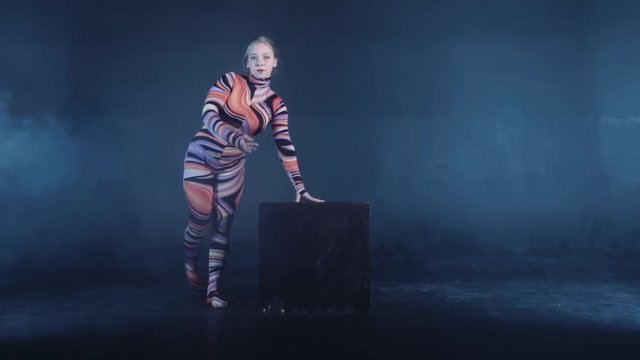 Young flexible blonde circus acrobat posing in studio in costume. Doing equilibre balance handstand on a cube. Copy space text.