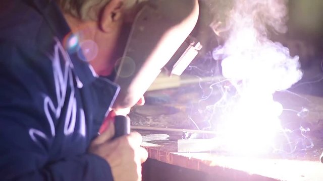 Mature welder welding two metal scraps in workshop