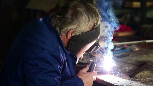 Mature welder welding two metal scraps in workshop