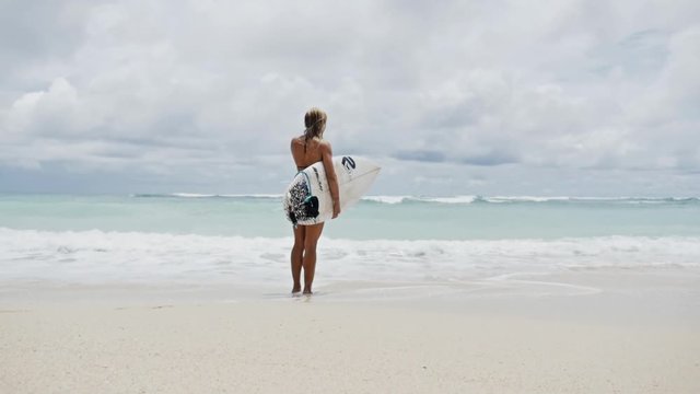 Slowmotion footage of a surfer girl checking the surf spot with her surfboard.