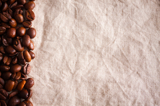 Coffee beans on left, empty space on right, on linen burlap background © avirid