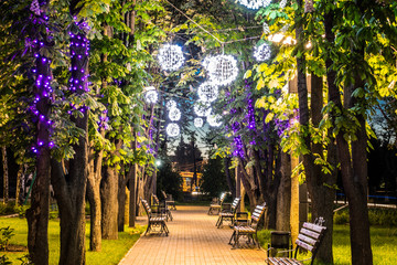 Narrow illuminated and decorated street with light spheres and sitting benches at summer. Night or dusk time