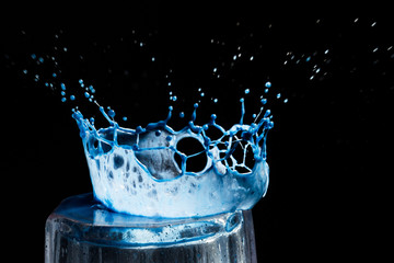Colorful close-up a blue drop in the form of a crown is split on the glass isolated on a black background