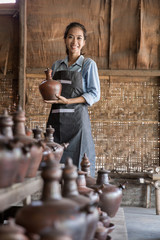 Smiling female potter proudly standing in her pottery workshop