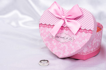 Heart shaped gift box with wedding ring over white satin