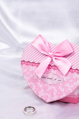 Heart shaped gift box with wedding ring over white satin