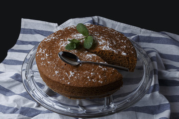 Chocolate cake with sugar decoration on glass stand on a dish towel
