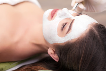 Spa concept. Young woman with nutrient facial mask in beauty salon, close up