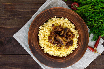 Eastern traditional wheat porridge - bulgur with roasted pieces fatty meats, bacon in a clay bowl on dark wooden background.  The top view