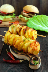 Baked potato circles on a bamboo skewer with spices (homemade chips). Snacks for beer on a dark wooden background.