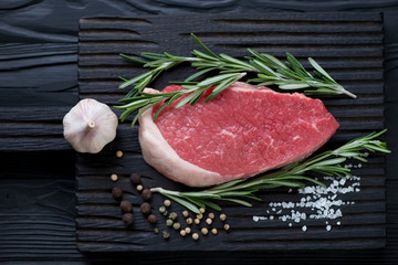 Black wooden chopping board with raw seasoned beef medallion