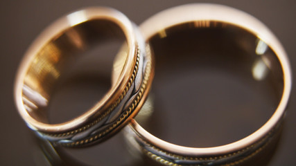 Golden wedding rings on mirror glasses table - one lies top of another, horizontal, macro