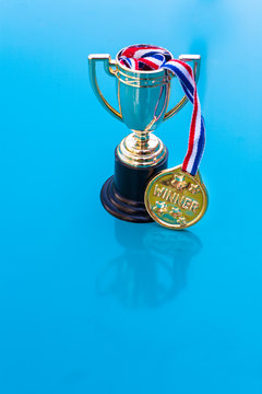 Gold trophy with winner medallion on red white and blue ribbon.