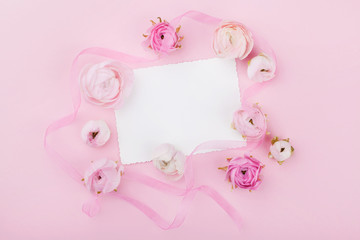 Fototapeta na wymiar White paper blank and spring flower on pink desk from above for wedding mockup or greeting card on womans day. Floral frame in flat lay style.