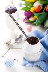 Easter egg filled with chocolate cake, tulips and colorful quail eggs on white background. Easter holidays breakfast concept.